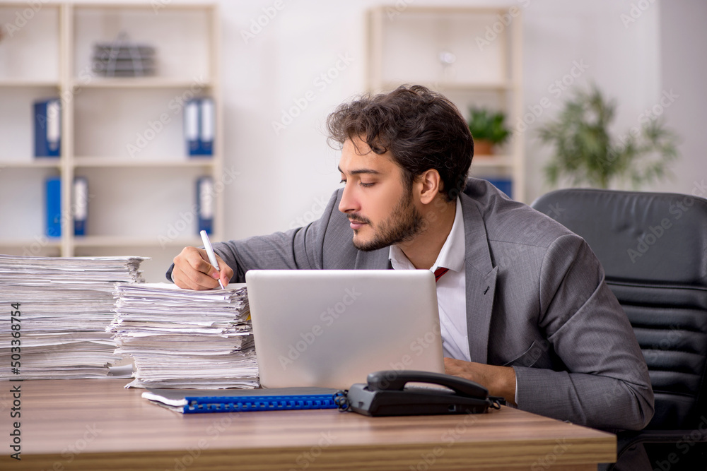 Young male employee unhappy with excessive work in the office Young male employee unhappy with excessive work in the office