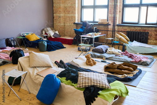 Large group of sleeping places with blankets, pillows, toys, sacks and other essentials prepared for refugees in spacious room