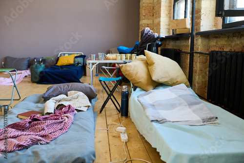 Two sleeping places of refugees with mattresses done with blankets or plaids in spacious room prepared for temporarily homeless people