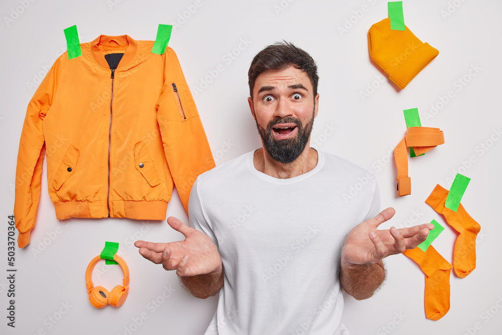 Φωτογραφία Puzzled hesitant adult man with thick beard spreads palms looks indignant cannot understand whats happening poses indoors against white background with plastered clothes behind