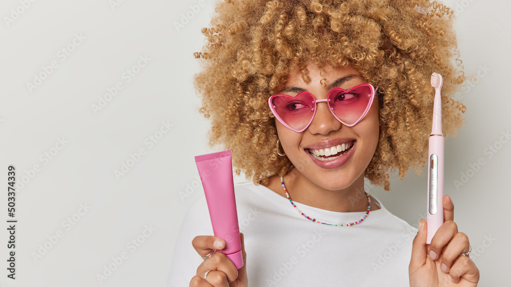 Positive carefree young woman holds toothpaste tube and electric