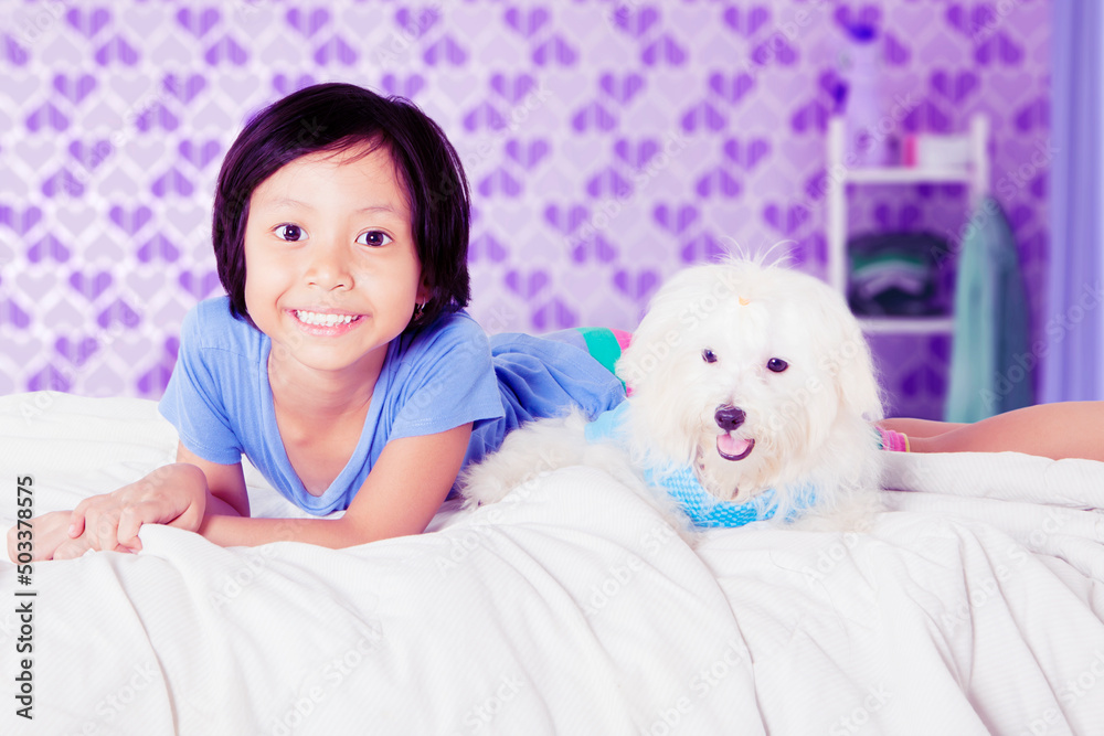 Happy little girl lying with maltese dog on bed Happy little girl lying with maltese dog on bed