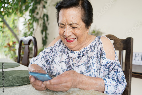 Happy elderly Hispanic woman using smartphone. Old Latina woman communicating with cellphone.  