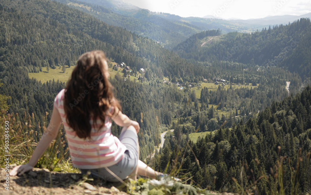 Young woman from behind is looking at mountain valley in summer day