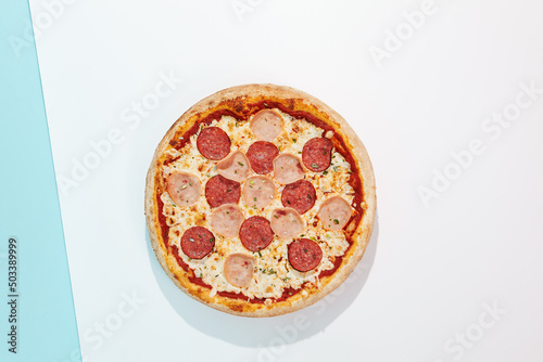 Italian pizza with ham and salami on coloured background. Meat pizza with ham and pepperoni in minimal style on light blue color. American pizza delivery concept with color backdrop