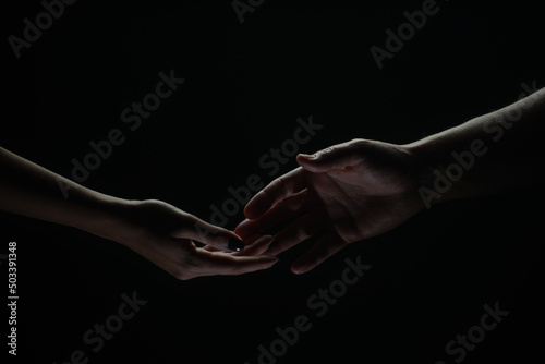 Two hands reaching toward. Helping hand outstretched for salvation on isolated black background. Close up of man and woman hand touch with fingers. Man and woman holding hands.