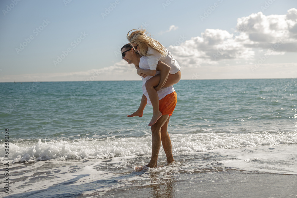 Boyfriend carrying lady on his back, couple enjoying romantic beach day Boyfriend carrying lady on his back, couple enjoying romantic beach day