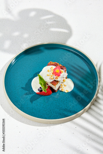 Carrot cake with cream cheese and berries on ceramic plate. Elegant dessert - carrot pie on white background with shadows of leaves. Portion cake on modern plate in minimal style.