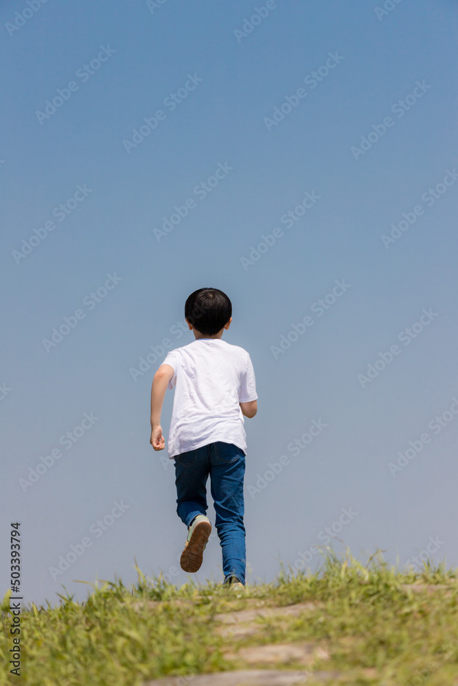 初夏の野原で遊んでいる小学生の男の子の姿