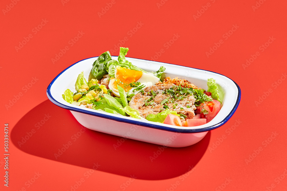 American cobb salad with chicken, eggs and vegetables in minimal style. Healthy salad on trend red background with hard shadow. Bowl with salad, chicken, eggs, vegetables in contemporary style American cobb salad with chicken, eggs and vegetables in minimal style. Healthy salad on trend red background with hard shadow. Bowl with salad, chicken, eggs, vegetables in contemporary style
