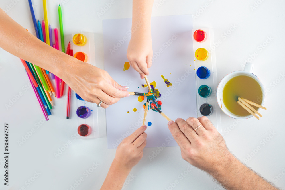 Hands of a family drawing with pencil and paints. Top view to white table with art supplies. Kids learning painting. Hands of a family drawing with pencil and paints. Top view to white table with art supplies. Kids learning painting.