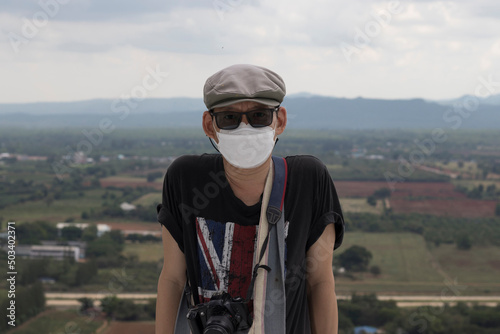 portrait one man carrying a camera Wearing a hat and sunglasses, wearing a mask behind the beautiful landscape cap, New normal and social distancing concept. © Monta