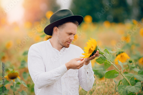 Young farmer man in hat inspects sunflowers field. Sunlight concept industrial