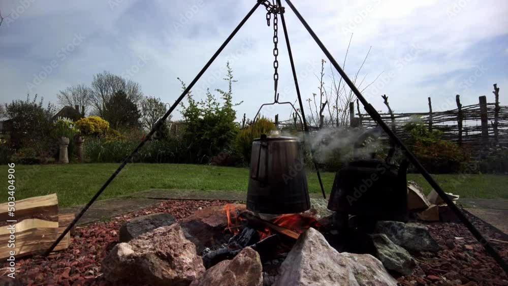 An old percolator coffee pot on a tripod boiling above the campfire, on the refractory cobblestones the tea water is heating in an old cast iron pot An old percolator coffee pot on a tripod boiling above the campfire, on the refractory cobblestones the tea water is heating in an old cast iron pot