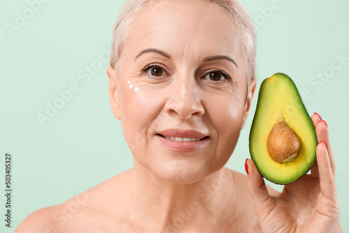 Mature blonde woman with avocado on green background