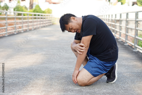 Asian middle-aged man fell down on the floor, feel hurt his knee and arm after running , jogging, exercise. Concept : injury accident in workout or sport. Copy space for text. 
