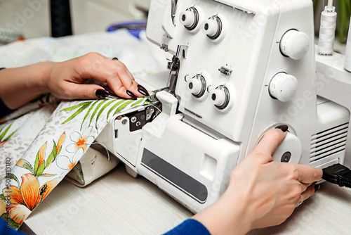 A woman seamstress fashion designer sews on a sewing machine overlock. Setting up the overlock sewing equipment at home. Hobbies at home. photo