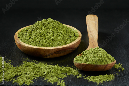 Closeup with bowl and wooden spoon with moringa powder on black background