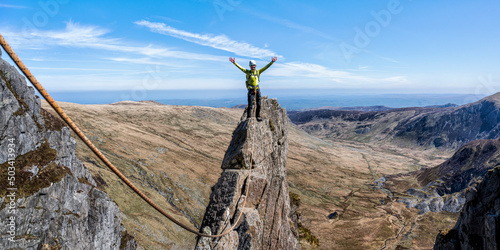 Active senior woman with arms raised standing on top of rocky mountain peak photo