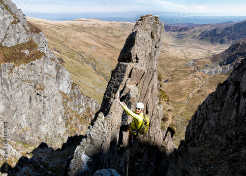 Smiling senior woman climbing rocky mountain cliff photo