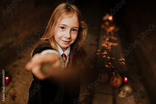 Blond girl with magic wand wearing witch costume standing in spooky tunnel