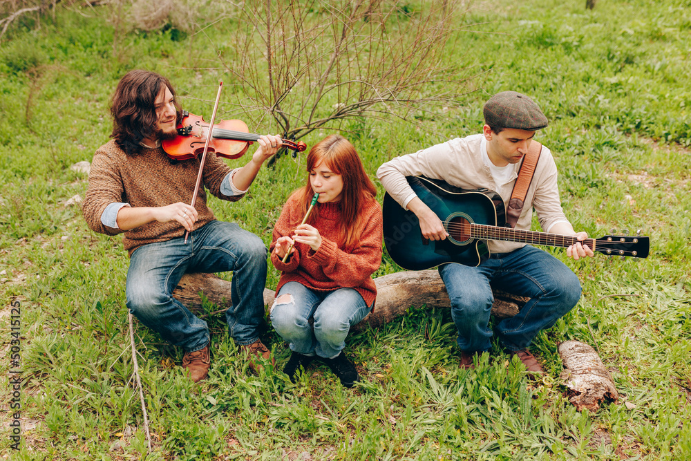 Artists practicing musical instruments sitting on log in field
