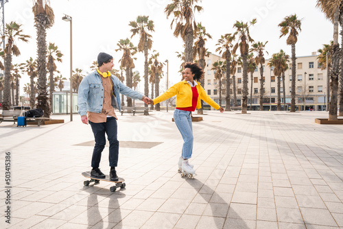 Happy couple holding hands skating together on footpath