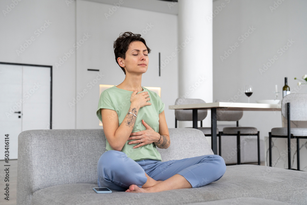 Woman with eyes closed meditating on sofa at home Woman with eyes closed meditating on sofa at home