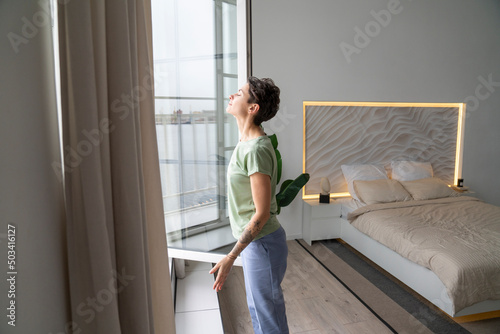 Woman with eyes closed breathing fresh air through window at home