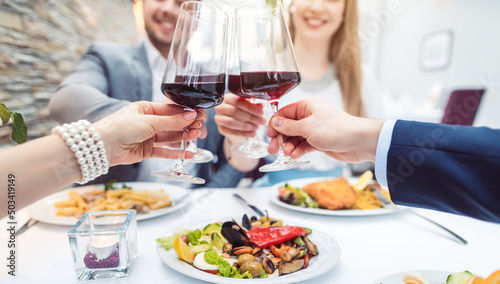 Close-up on hands of patrons in restaurant with glasses of red wine over table with food