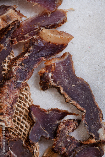 South African Biltong, a dried and cured meat sliced and on grey backdrop with copy space