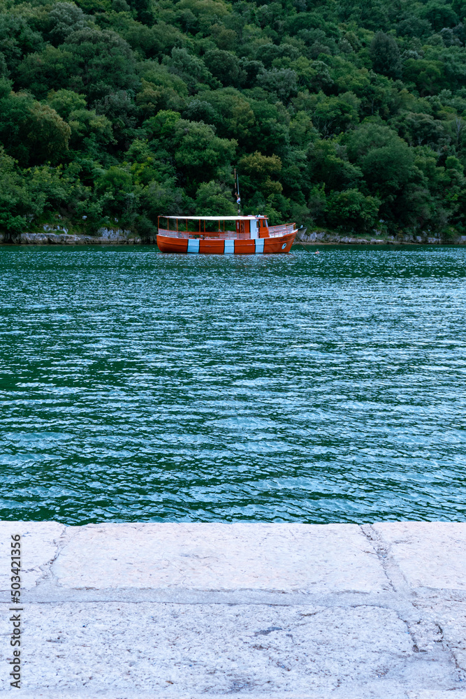Naklejka premium Red boat on water, with forest background, nearby shore.