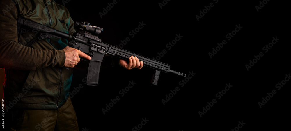 A man in dark clothes holds an automatic carbine in his hands. The face is covered with a mask, hands are in gloves. A figure with a weapon on a dark background A man in dark clothes holds an automatic carbine in his hands. The face is covered with a mask, hands are in gloves. A figure with a weapon on a dark background