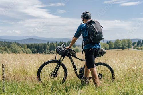 Bikepacking in the mountains. Man standing on a meadow with his bike and backpack ready for a bikepacking adventure ride.