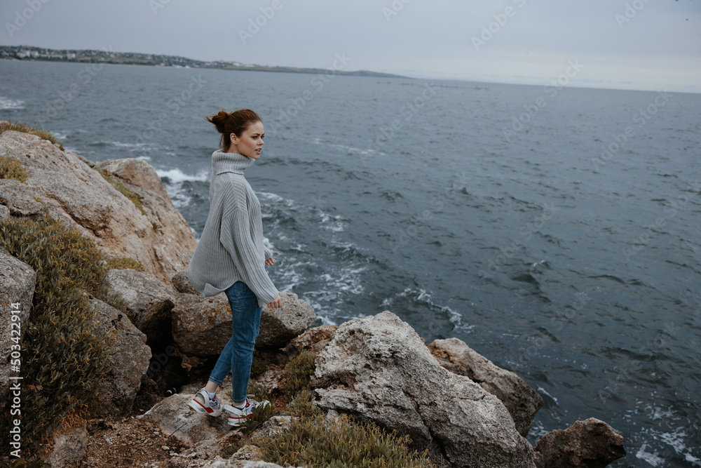 beautiful woman in a gray sweater stands on a rocky shore nature Relaxation concept