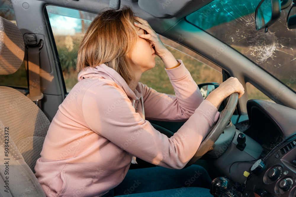 A sad woman is sitting behind the wheel of a car and holding her head with her hand. A sad woman is sitting behind the wheel of a car and holding her head with her hand.