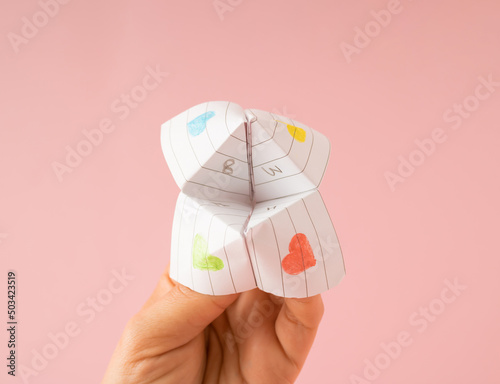 Paper origami fortune teller in hand against pink background. Minimal concept.