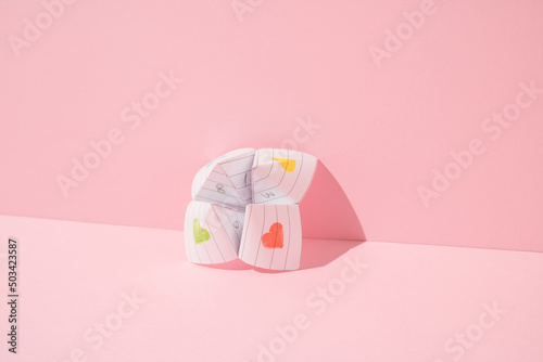 Paper origami fortune teller leaning against pink background. Minimal concept. photo
