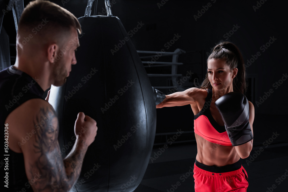 Athletic woman in red shorts and top is boxing with a trainer. Boxing and mixed martial arts concept.