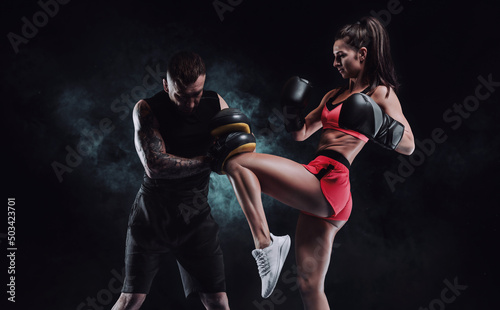 Athletic woman in red shorts and top is boxing with a trainer. Boxing and mixed martial arts concept. © andy_gin