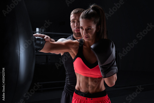 Athletic woman in red shorts and top is boxing with a trainer. Boxing and mixed martial arts concept. © andy_gin