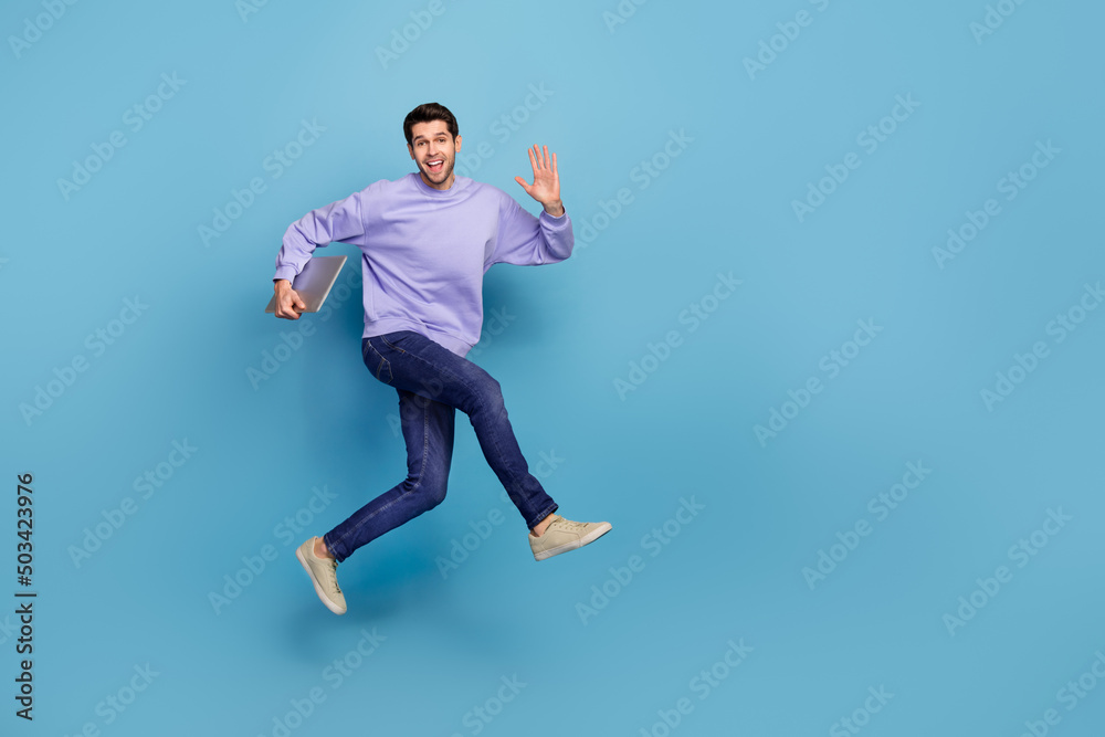 Full length body size view of attractive cheerful guy jumping carrying laptop waving hi hello isolated over bright blue color background