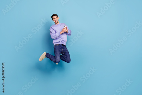 Photo of millennial blogger guy jump use device enjoy network ads apps isolated pastel blue color background © deagreez