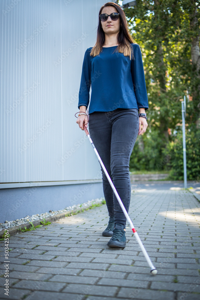 Blind woman walking on city streets, using her white cane to navigate the urban space better and to get to her destination safely Blind woman walking on city streets, using her white cane to navigate the urban space better and to get to her destination safely