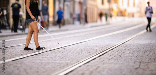 Blind woman walking on city streets, using her white cane to navigate the urban space better and to get to her destination safely