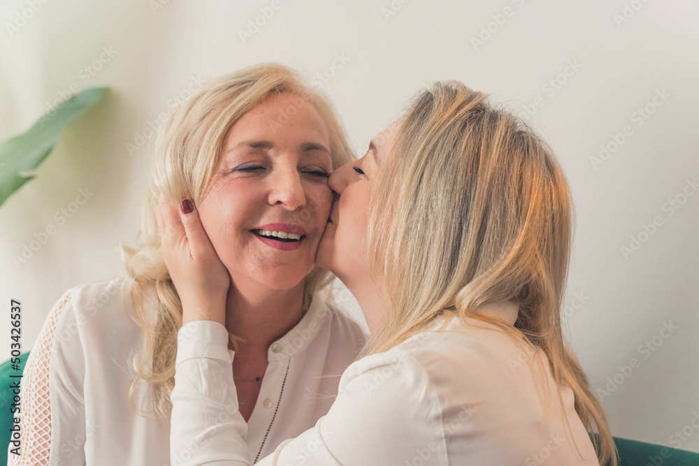 Happy mature mother and grown-up adult daughter hugging share close intimate moment together, smiling elderly mom and millennial girl child, grown-up daughter kissing her mom. High quality photo Happy mature mother and grown-up adult daughter hugging share close intimate moment together, smiling elderly mom and millennial girl child, grown-up daughter kissing her mom. High quality photo