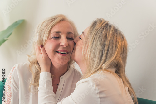 Happy mature mother and grown-up adult daughter hugging share close intimate moment together, smiling elderly mom and millennial girl child, grown-up daughter kissing her mom. High quality photo
