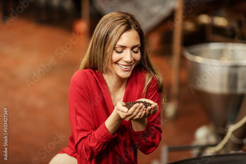 A happy woman holding and smelling fresh coffee beans in coffee factory.