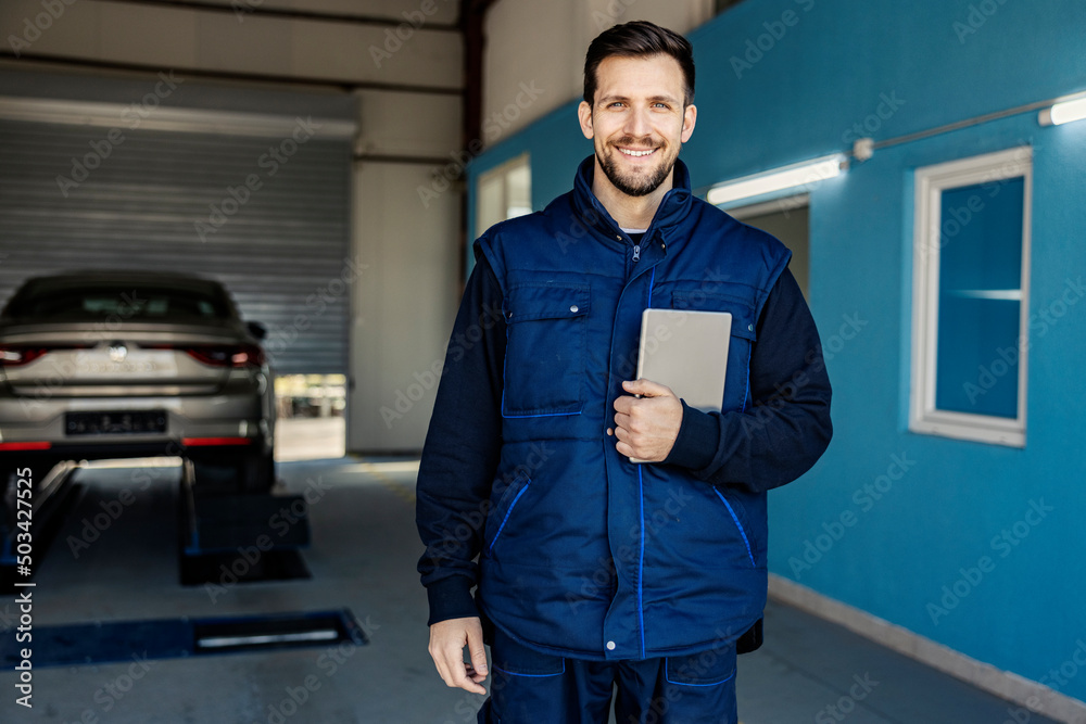 A successful car mechanic's shop worker holding tablet in hands and smiling at the camera. A successful car mechanic's shop worker holding tablet in hands and smiling at the camera.