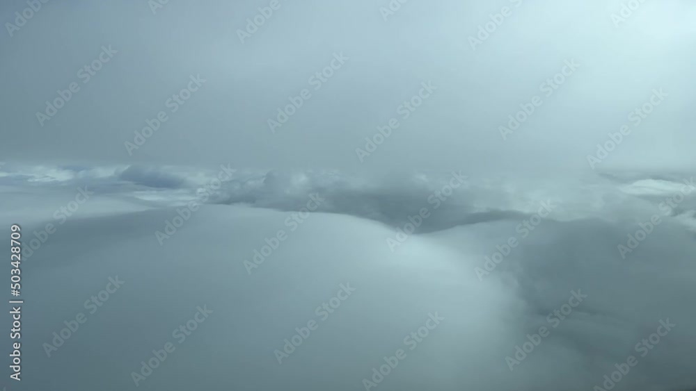 Aerial view from a jet cockpit while flying between layers of soft white and grey clouds Aerial view from a jet cockpit while flying between layers of soft white and grey clouds